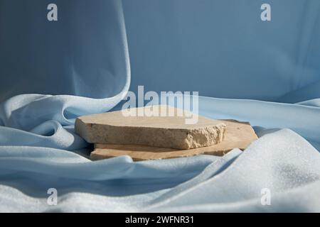 Podium en pierre cassée décoré sur fond luxueux de texture de tissu bleu clair. Scène vierge, plate-forme ou socle pour produit de présentation. Banque D'Images