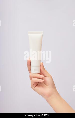 Modèle de main femelle tenant un tube blanc d'étiquette vide sur fond blanc. Concept de crème de produits de beauté Banque D'Images