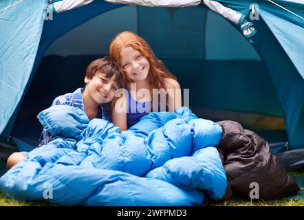 Portrait, camping et enfants s'embrassent dans un sac de couchage de tente avec amour, soin et lien dans la nature ensemble. Famille heureuse, enfants et frères et sœurs se réveillent Banque D'Images