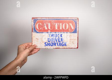 Pénurie de camionneurs. Signe d'avertissement en métal dans la main d'une femme sur un fond blanc. Banque D'Images