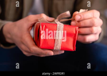 Gros plan mains d'homme ouvrant un cadeau de Saint-Valentin avec un arc. Banque D'Images