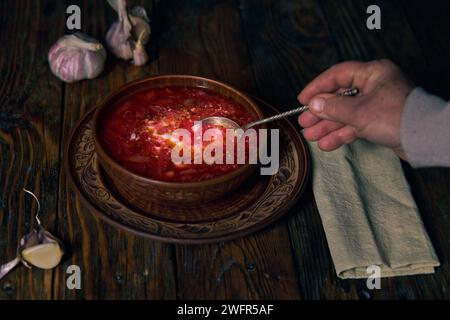 National ukrainien borscht, faïence, borscht avec de la crème sure dans une assiette, une main humaine écale borscht avec une cuillère d'une assiette, ail, serviette sur Banque D'Images