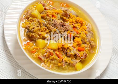 soupe fendue de pois et de lentilles avec porc sur os et légumes dans un bol blanc sur une table en bois blanc, gros plan Banque D'Images