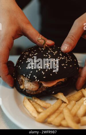 Mains masculines tenant un hamburger de bœuf avec un petit pain noir dans un café. Délicieux déjeuner américain Banque D'Images