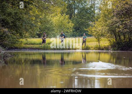 Trois pêcheurs à la ligne profitant de la pêche entouré par la nature verdoyante de la rive de la rivière. Passe-temps extérieur et concept d'activité. Banque D'Images