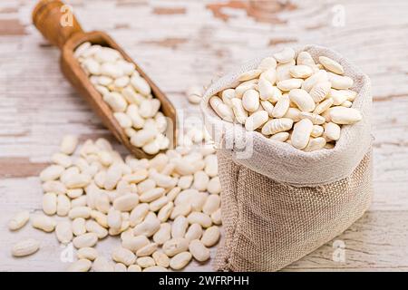 Gros plan de haricots renversés d'un sac en toile de jute sur une surface en bois rustique. Banque D'Images