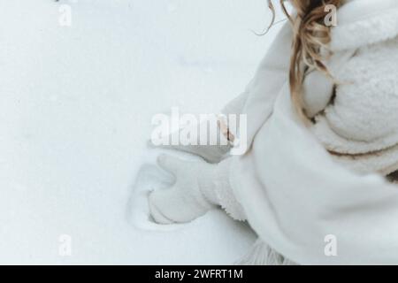 Les mains de la femme en mitaines blanches prenant la neige, faisant boule de neige. Banque D'Images