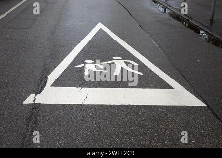 Attention : enfants jouant - panneau de sécurité urbain sur chaussée mouillée. Banque D'Images