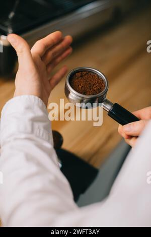 La main du barista tient un support avec du café frais moulu pour préparer du café dans une machine à café. Gros plan. Banque D'Images