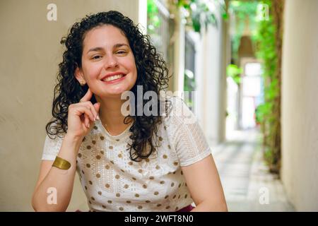 Heureuse jeune femme latine d'ethnie vénézuélienne avec des curleurs élégants, assis calmement souriant regardant la caméra, se sentant satisfaite, espace de copie. Banque D'Images