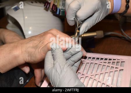 Le manucure tient les mains du client dans ses propres mains et utilise des pinces pour couper la vieille peau des ongles. Banque D'Images