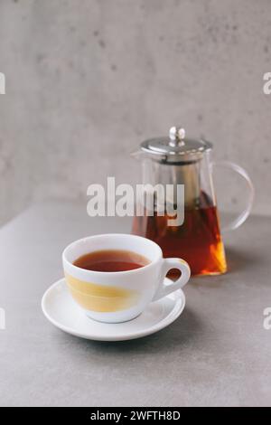 Théière en verre et tasse avec thé aromatique isolé sur fond gris. Banque D'Images