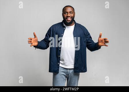 Un homme afro-américain joyeux se tient debout avec les bras tendus, mesurant ou présentant quelque chose d'invisible debout isolé sur fond gris. L'homme noir tient un objet imaginé, quelque chose dans les paumes Banque D'Images