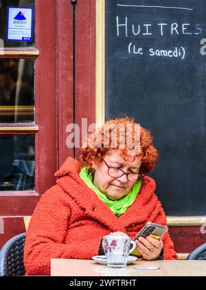 Femme avec des cheveux de gingembre / o-gamme assis à la table de visage et regardant smartphone - Tours, Indre-et-Loire (37), France. Banque D'Images