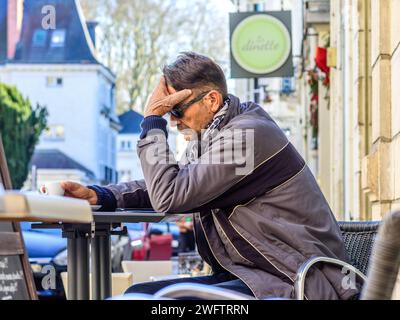 Homme pensif assis à la table de café en plein air à l'aide d'un smartphone - Tours, Indre-et-Loire (37), France. Banque D'Images