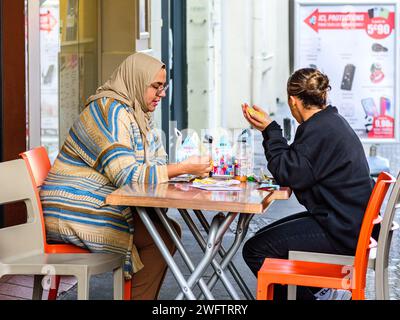 Deux femmes (une arabe) mangeant à table de café en plein air - Tours, Indre-et-Loire (37), France. Banque D'Images