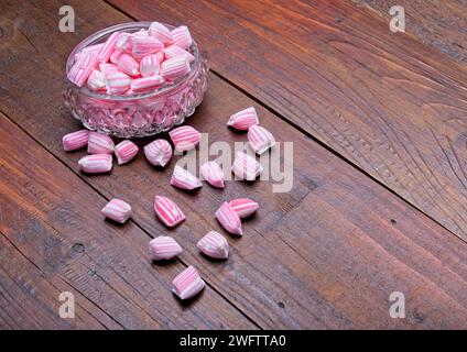 Bonbons rayés roses et blancs dans un petit bol en verre sur une surface en bois brun avec espace de copie Banque D'Images