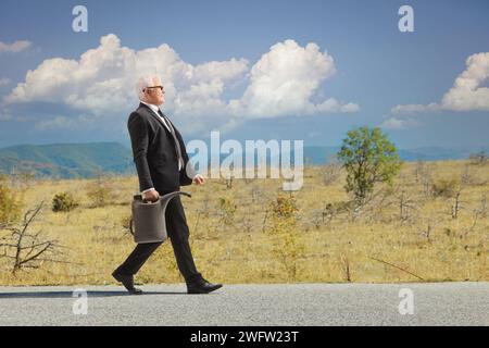 Homme seul sur une route ouverte marchant et portant une cartouche d'essence Banque D'Images