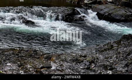 Eau turbulent blanche et sarcelle de la rivière se précipitant sur les roches noires. Banque D'Images