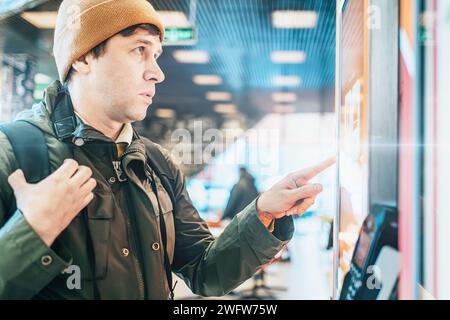 Jeune homme utilisant le terminal libre-service avec grand écran de capteur pour acheter la restauration rapide dans le restaurant ou en cours d'achat de billet de la machine automatisée. Banque D'Images