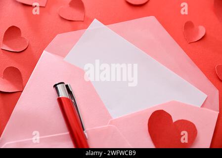 Détail de l'enveloppe ouverte avec lettre vierge sur fond rouge et avec découpes de coeurs et stylo. Vue de dessus. Banque D'Images