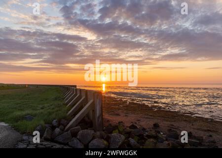 Digue en bois à la mer des Wadden (patrimoine mondial de l'UNESCO) pendant le coucher de soleil coloré Banque D'Images