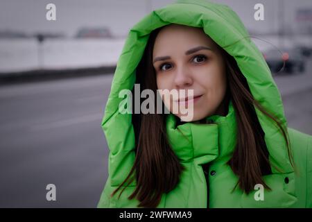 Femme en manteau vert debout sur le côté de la route en hiver. Banque D'Images