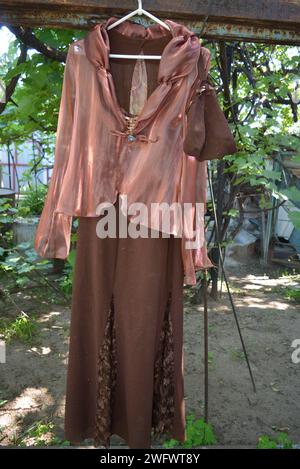 La vie ordinaire, le style, la mode, belle robe marron pour femmes avec veste en organza rouge brun accrochée sur un cintre blanc dans la cour de la maison. Banque D'Images