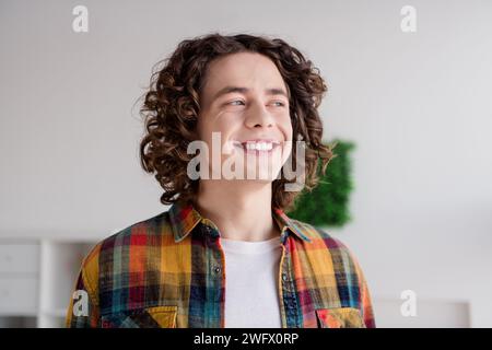 Photo de rêveur mec de bonne humeur habillé chemise à carreaux souriant dents blanches rêvant à l'intérieur maison chambre à la maison Banque D'Images