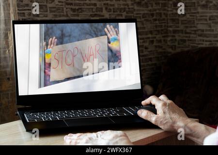 Une fille dans la fenêtre de la maison tient une affiche Stop the war et un drapeau peint de l'Ukraine dans ses mains, comme on le voit sur la photo d'un ordinateur portable à la maison Banque D'Images