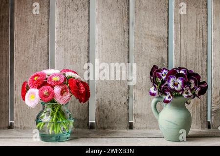 Bouquets de pensées et fleurs de Marguerite dans des vases en céramique. Fond en bois avec espace de copie. Banque D'Images