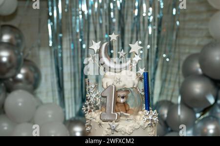 Gâteau encadré avec forme de croissant de lune et étoiles sur le dessus plus petit ours en peluche brun, pour le premier anniversaire. Encadré par des ballons blancs et argentés. Banque D'Images