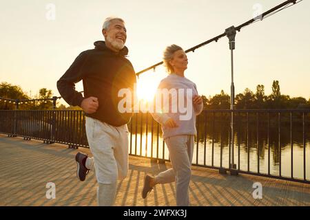 Sportif senior couple souriant dans sportswear jogging le long d'un pont dans le parc ayant l'entraînement sportif. Banque D'Images