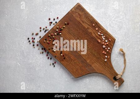 grains de poivre éparpillés et sel rose sur une planche à découper en bois brun sur une table en pierre blanche Banque D'Images