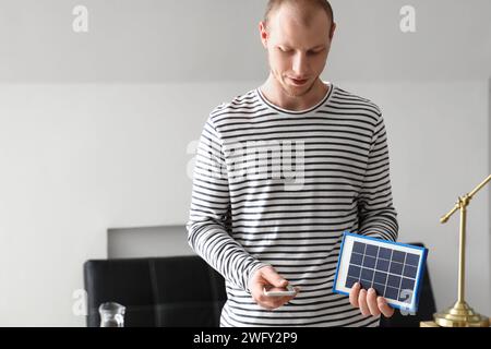 Jeune homme utilisant le téléphone portable de charge à partir de panneau solaire portable à la maison Banque D'Images