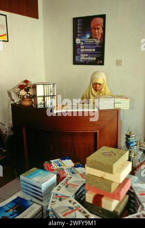 Une femme travaille derrière une caisse, devant un mur où une photo du fondateur de Daarut Tahiid, le chef religieux islamique indonésien KH Abdullah Gymnastiar (populairement connu sous le nom de AA Gym), est placée dans une librairie près de la mosquée Daarut Tauhiid à Gegerkalong, Bandung, Java Ouest, Indonésie. Fondée par KH Abdullah Gymnastiar, l'internat et la fondation Daarut Tauhiid, ainsi que leur direction de branche, Manajemen Qolbu (MQ), ont réussi à intensifier le tourisme religieux et les activités économiques dans la région de Gegerkanong dans la ville de Bandung. Banque D'Images
