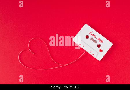 Cassette audio avec bande lâche formant un coeur sur fond rouge. Concept d'amour minimal. Carte d'amour créative à technologie rétro. esthétique des années 80. Banque D'Images