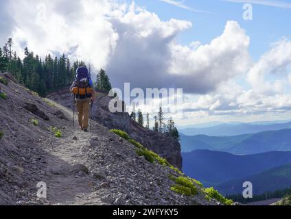 Homme dans ses années 50 randonnée sur une pente rocheuse en fin d'après-midi. Un matelas et un équipement de camping peuvent être vus attachés à son sac à dos. Banque D'Images