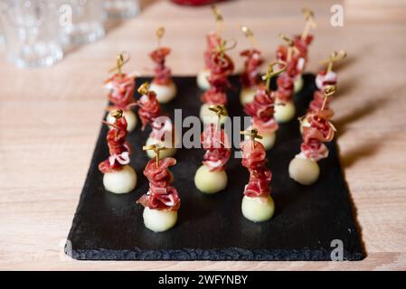 Élégants apéritifs melon et prosciutto sur cure-dents, magnifiquement disposés sur une planche en ardoise noire pour une fête. Banque D'Images