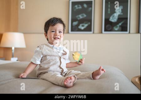 Mignon bébé garçon multiracial d'un an célébrant son premier anniversaire à la maison. Il est vêtu d'un costume en lin beige d'été avec un noeud papillon lumineux. Il l'est Banque D'Images