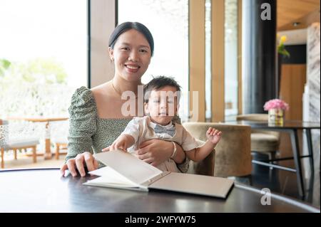 Mignon bébé garçon multiracial d'un an célébrant son premier anniversaire avec sa belle mère souriante dans un restaurant prêt à commander de la nourriture Banque D'Images