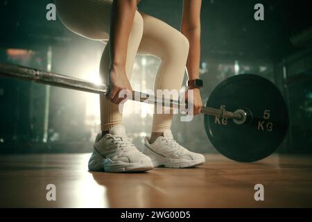 Jeune femme faisant le soulevé de terre avec la barre lourde dans la salle de gym, athlète féminine forte avec le corps musclé soulevant des poids, l'exercice avec barre. Banque D'Images