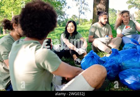 Groupe multiethnique de volontaires se reposant après le nettoyage du parc de la ville. Banque D'Images