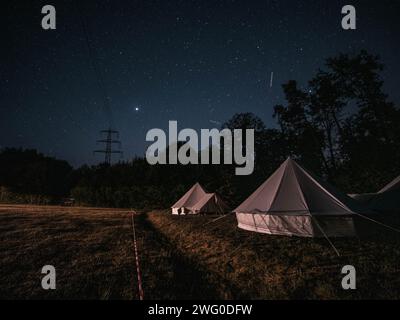 Deux tentes blanches nichées dans un champ herbeux entouré d'arbres sous un ciel étoilé, évoquant une ambiance sereine et paisible. Banque D'Images