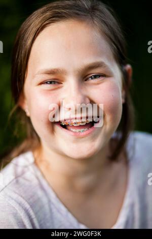 Portrait d'une fille de 12 ans riant en montrant ses bretelles. Banque D'Images