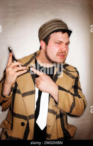 Jeune homme branché pointant son téléphone portable avec une expression ennuyée sur son visage. Banque D'Images