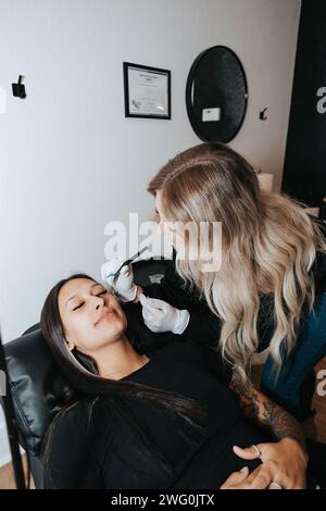 Artiste blonde, maquillage permanent pour client en chaise Banque D'Images