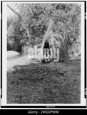 Glands de cuisine-Upper Lake Pomo, c1924. Femme indienne Pomo cuisinant devant un tipi de canne, Californie. Banque D'Images