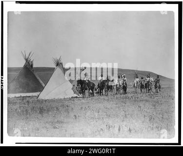 Un rassemblement de guerre, c1908. Paysage avec quatre tipis, onze Indiens Atsina à cheval, trois femmes, un enfant et deux chiens, Montana. Banque D'Images