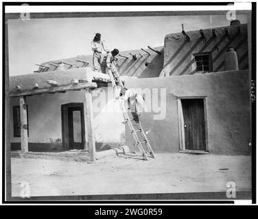 À San Ildefonso, c1927. Trois Indiens Tewa, deux sur le toit d'un bâtiment en adobe, un sur l'échelle, San Idlefonso, Nouveau Mexique. Banque D'Images